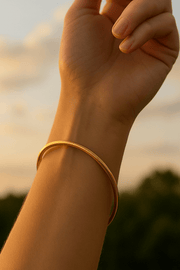 Hand wearing a gold bangle with a blurred natural background