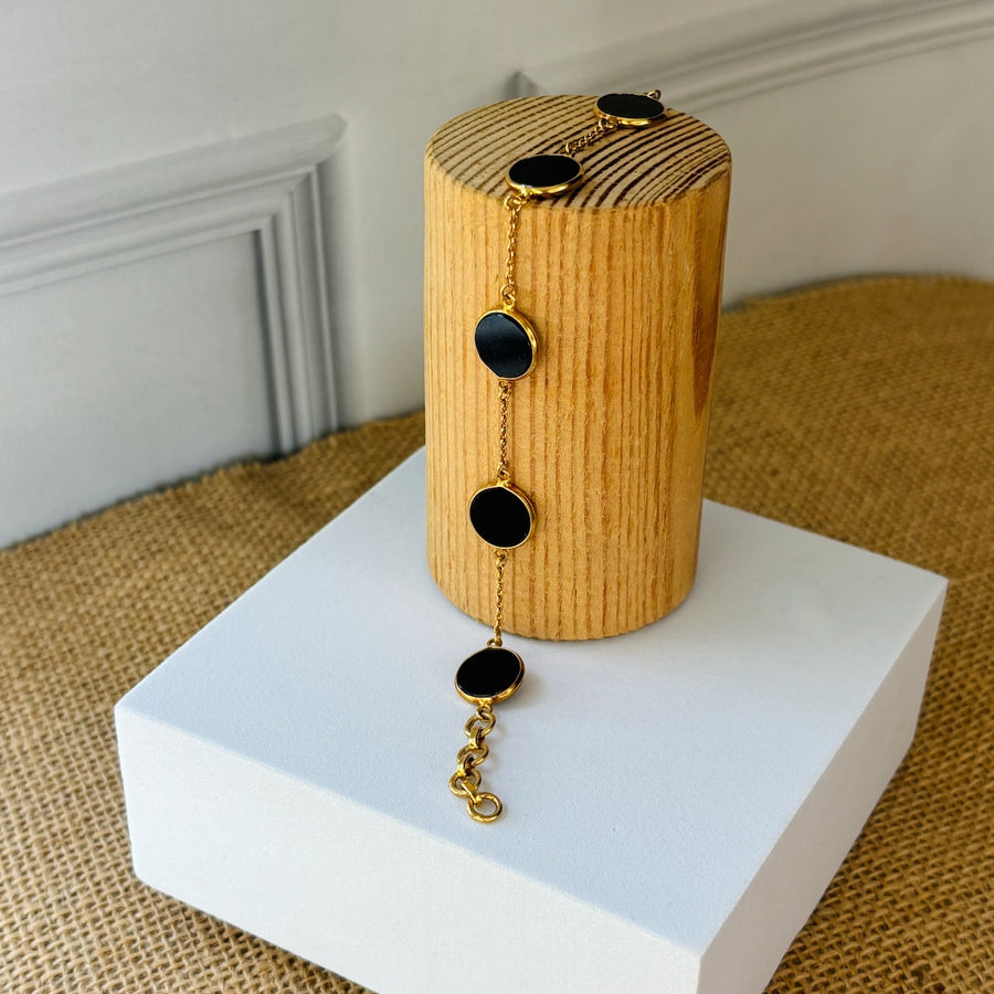 Carbon Bracelet - Black Onyx Beads displayed on a wooden stand, featuring distinct black onyx beads and gold accents.