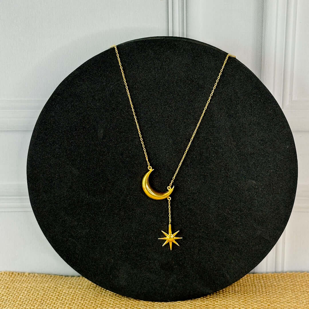 A gold-toned necklace with a crescent moon and a star design displayed on a black background.