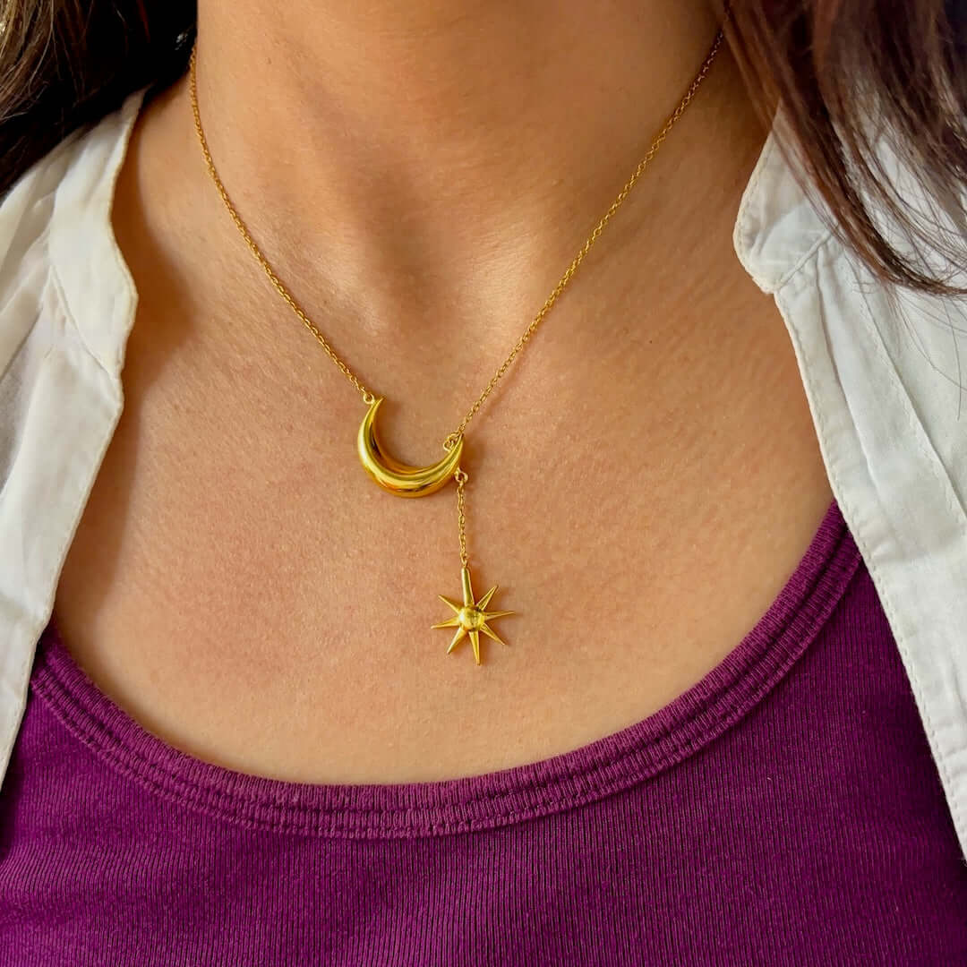A gold-toned necklace with a crescent moon and a star design worn by a model