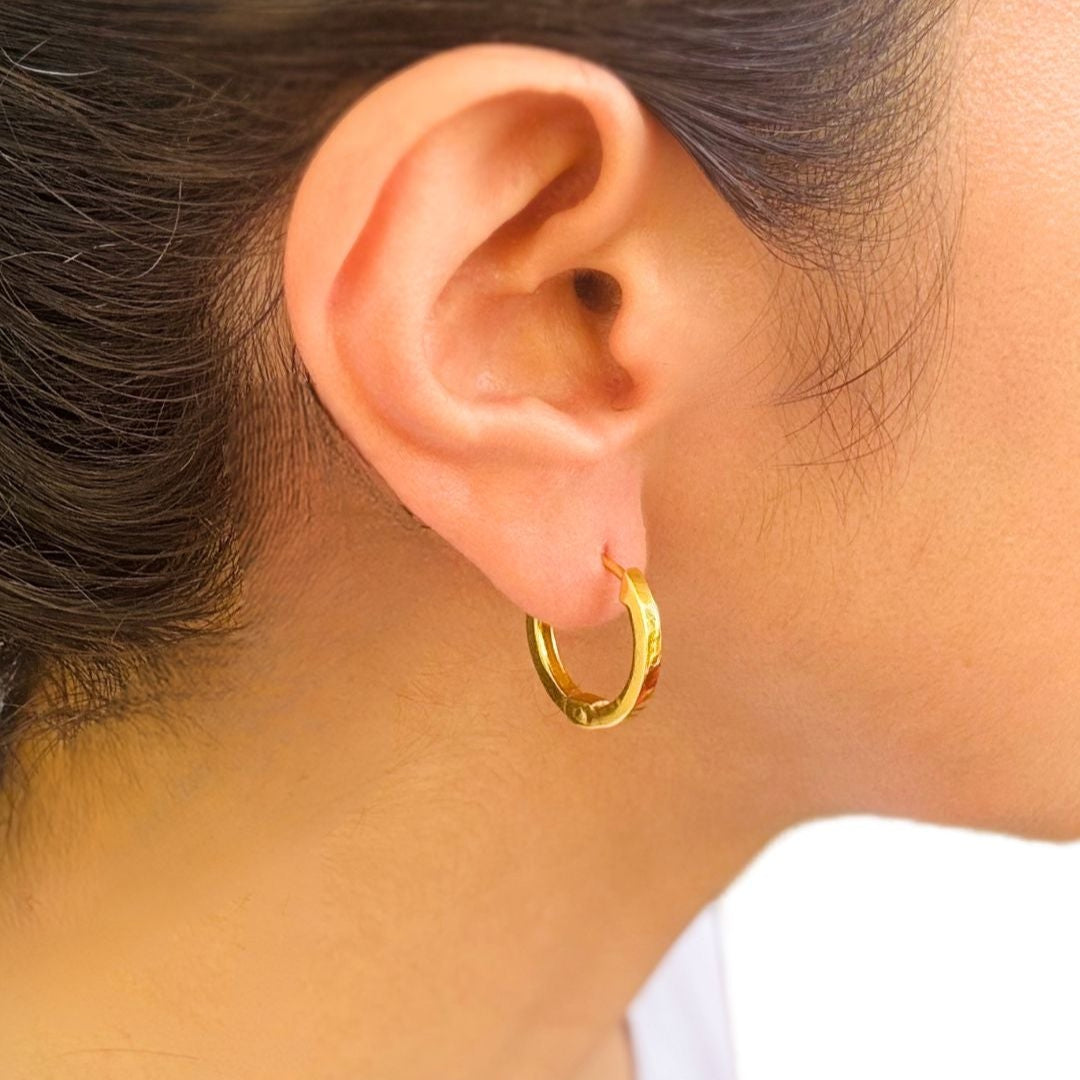 A person wearing a single gold-colored hoop earring on their ear lobe.