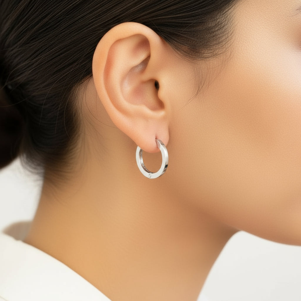 A person wearing a single gold-colored hoop earring on their ear lobe.