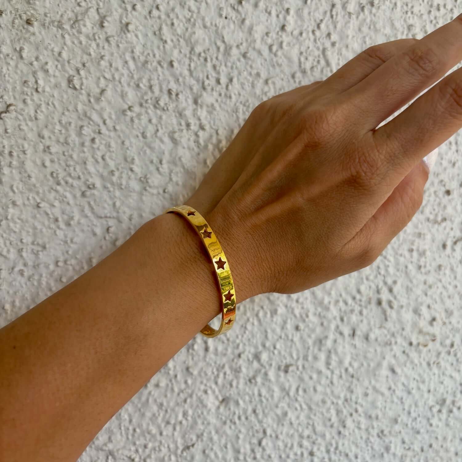 Hand wearing the Astra Star Bangle, showcasing its gold finish and star cutouts, adding celestial charm.