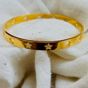 Astra Star Bangle resting on a white cloth, featuring gold finish with star cutouts, perfect for adding celestial charm.