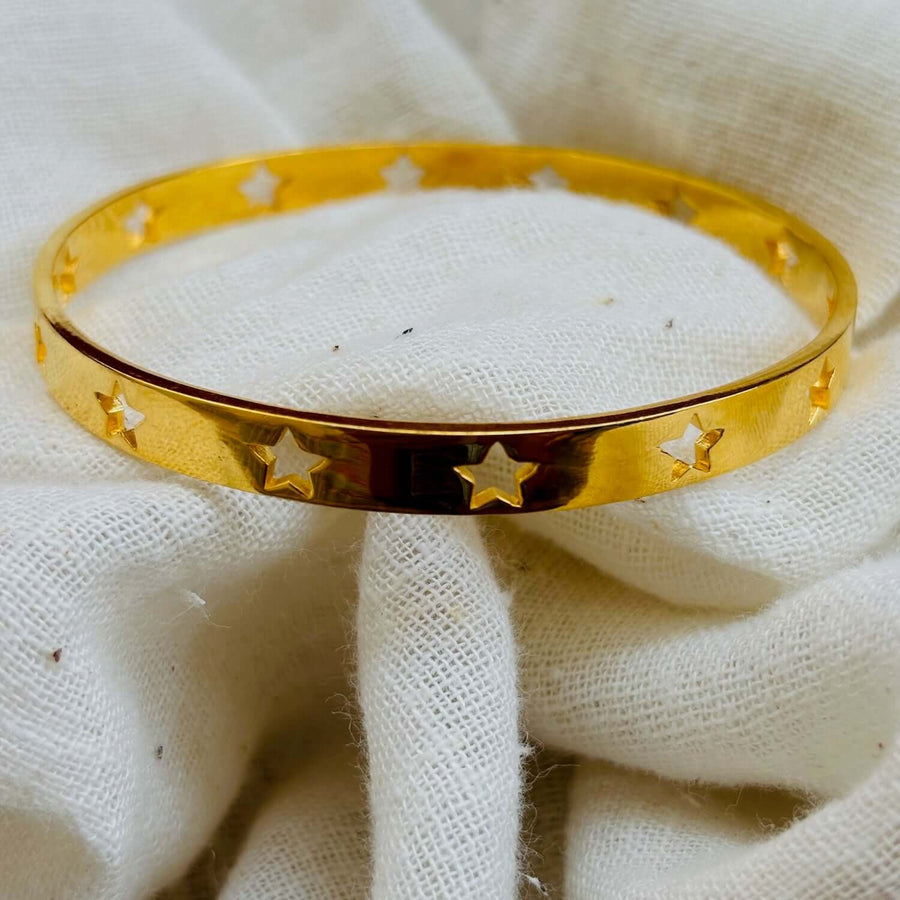 Astra Star Bangle resting on a white cloth, featuring gold finish with star cutouts, perfect for adding celestial charm.