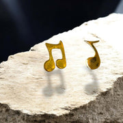 Gold music note earrings on a rock with a dark background