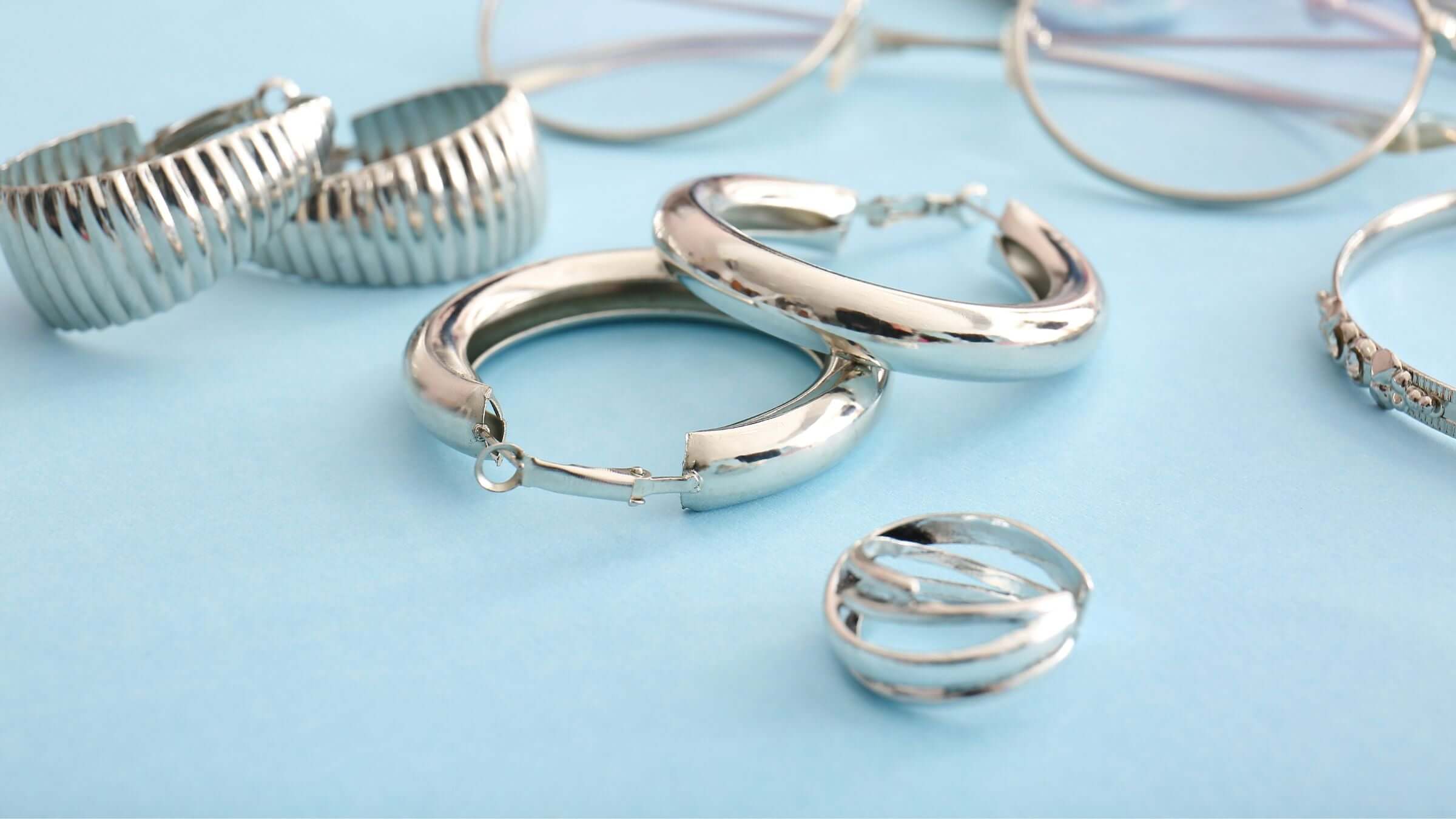 Stylish silver jewellery fashion featuring hoop earrings and rings on a light blue background.