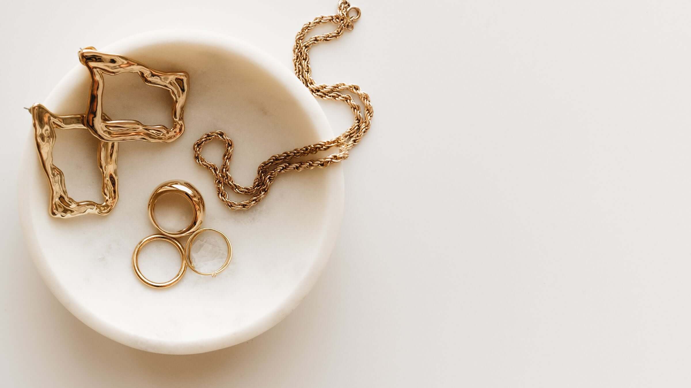 Elegant display of silver gold-plated jewellery benefits including rings and chains on a white plate.