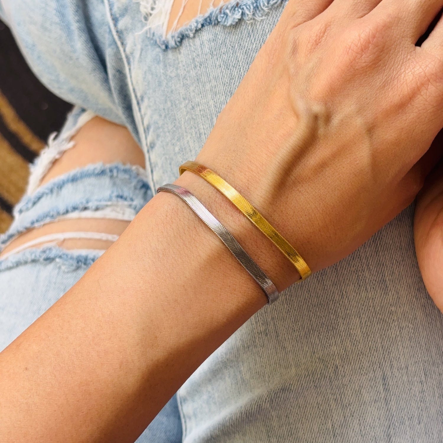 Close-up of a person's wrist wearing two bracelets, one gold and one silver, with a blurred background.