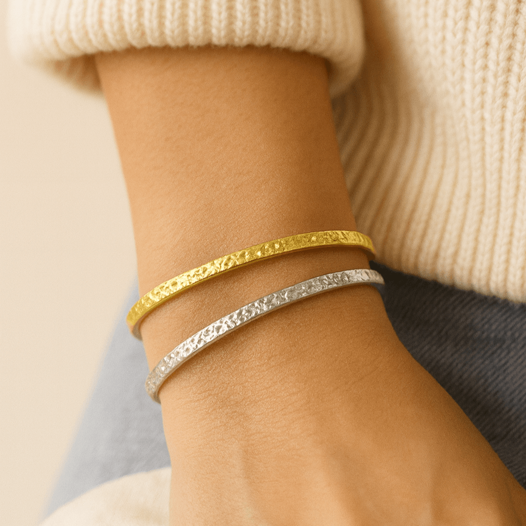 Close-up of a wrist wearing gold and silver bracelets against a neutral background