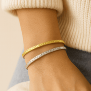 Close-up of a wrist wearing gold and silver bracelets against a neutral background