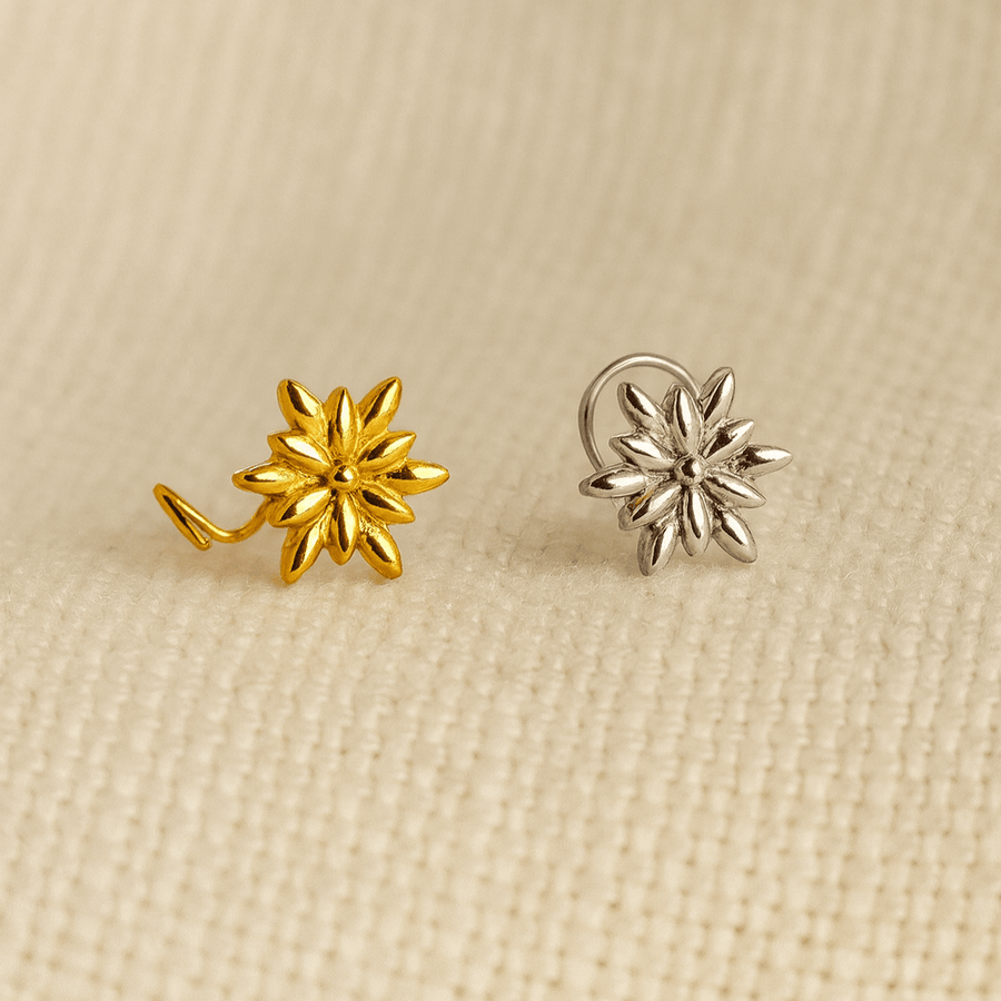 Gold and silver flower-shaped nose pins on a beige fabric background