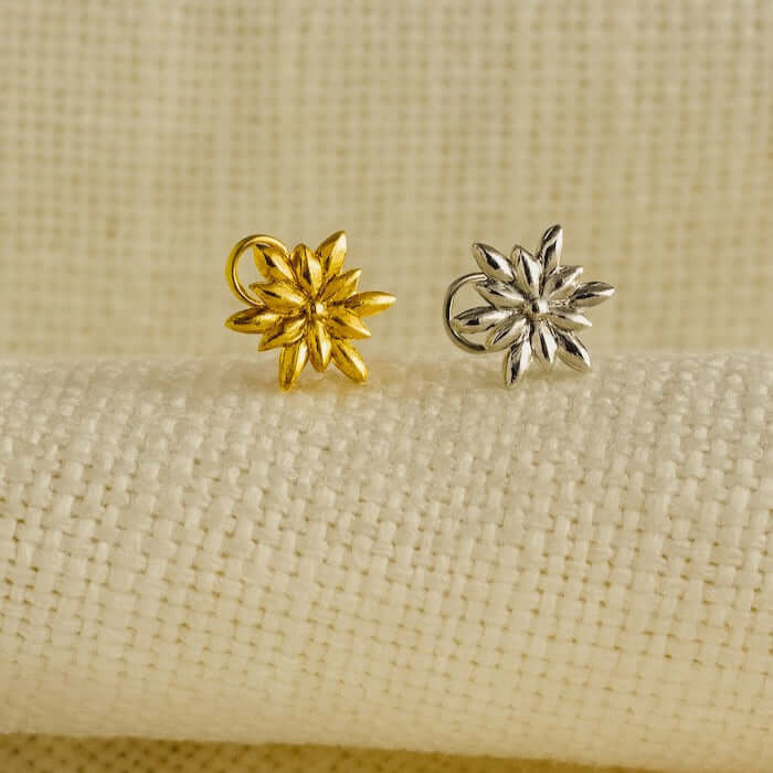 Gold and silver flower-shaped nosepins on a beige fabric background