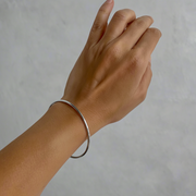 A gold-colored bangle bracelet worn on a person's wrist, showing a sleek, shiny finish.