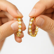 Celeste diamond hoops held between two fingers, showcasing round-cut cubic zircons in a gold vermeil finish.