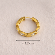 Gold hoop earring on a textured beige background with measurement label