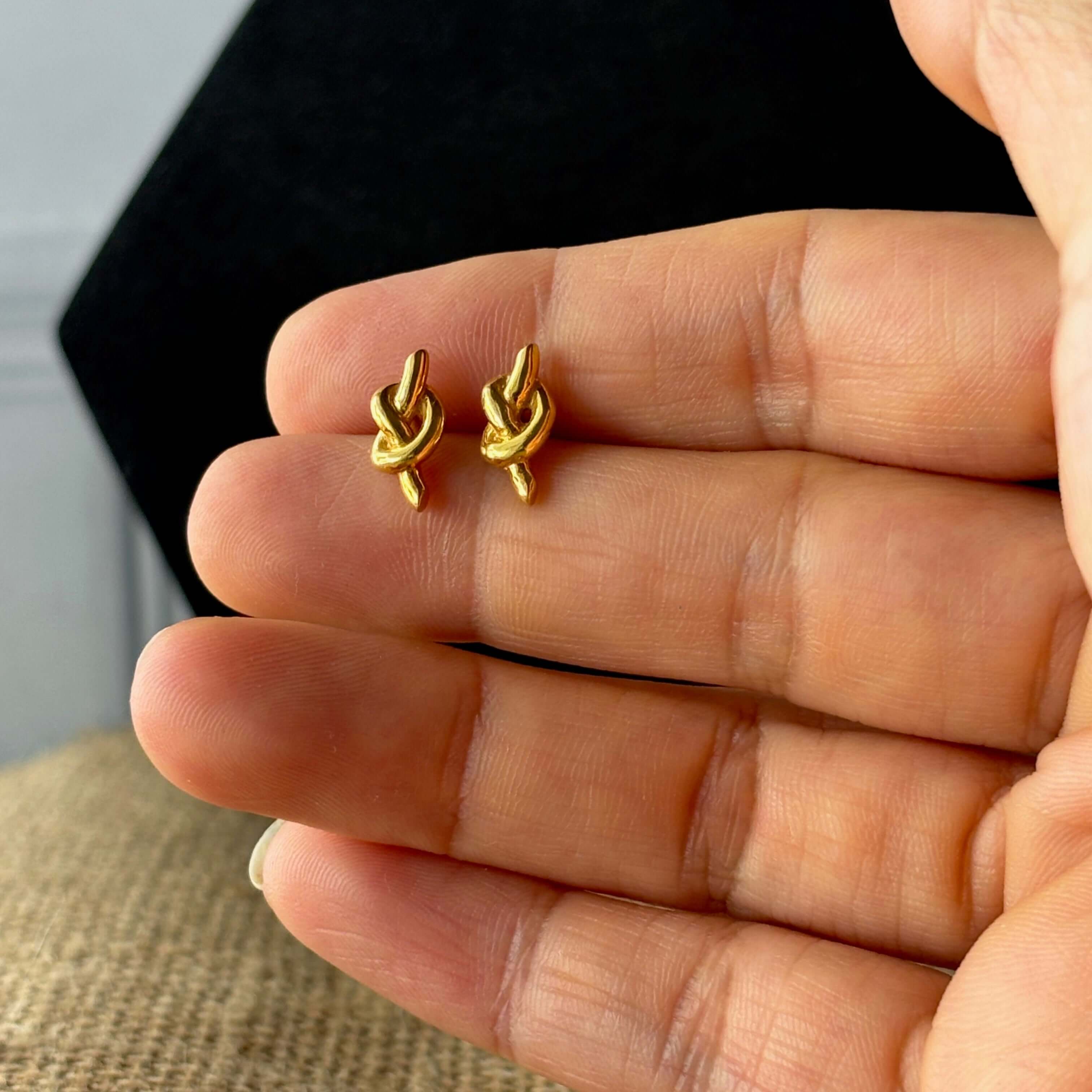 Knot Earring Studs held between fingers against a neutral background