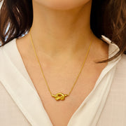 Gold necklace with a knot pendant worn by a person against a neutral background