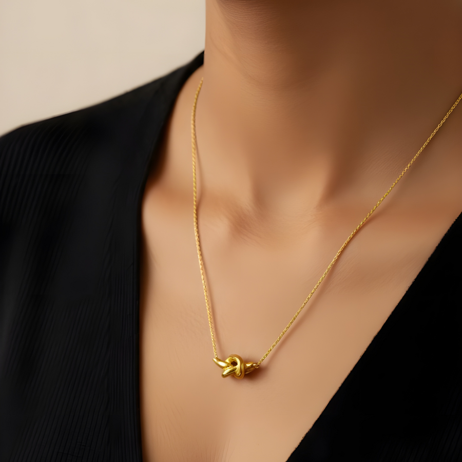 Gold necklace with a pendant on a person wearing a black top against a beige background