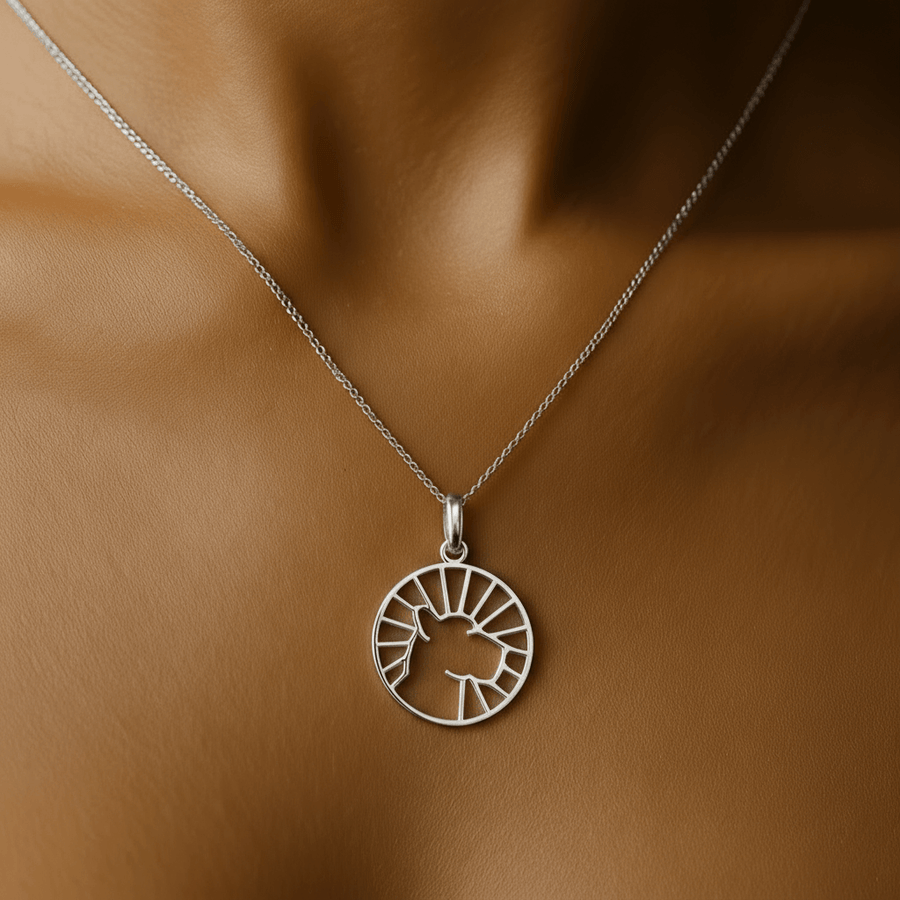 Gold necklace with a circular pendant on a person's neck against a dark background