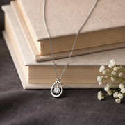 Silver necklace with a teardrop pendant on a stack of books with flowers.