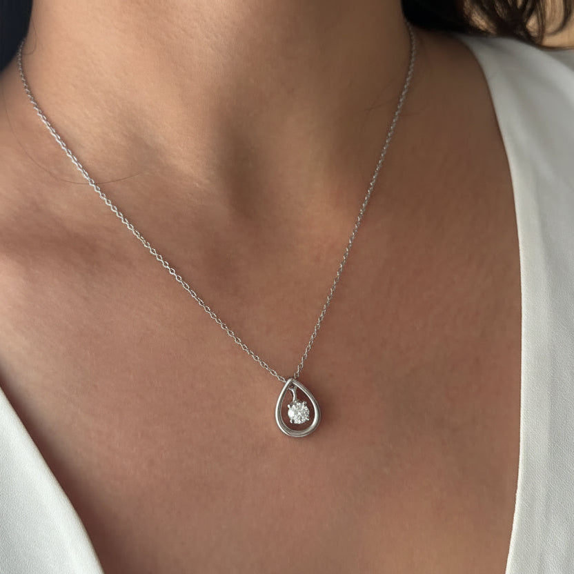 Gold necklace with a teardrop pendant on a person wearing a white top.