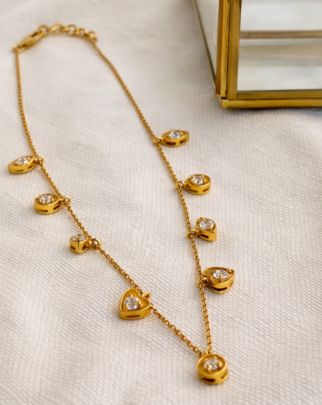 Gold necklace with heart-shaped pendants on a beige fabric background
