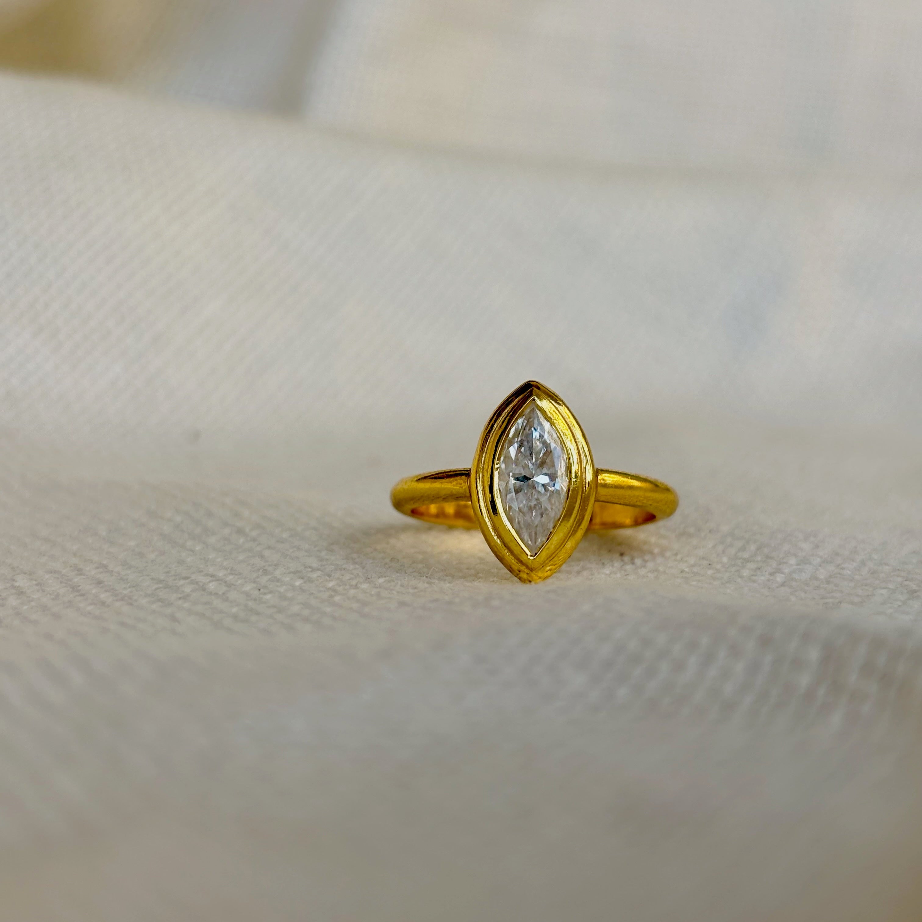 Gold ring with a diamond on a beige fabric background