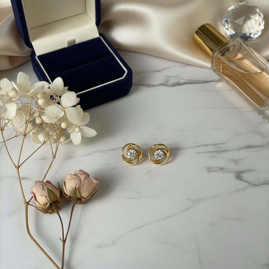 Gold earrings with diamond-like stones on a beige fabric background