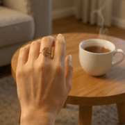 Hand with a Selena-Moon Charm Ring ring on a wooden table with a cup of coffee, blurred background